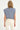 Woman wearing a blue and grey striped sleeveless top and beige pants on a white background