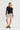 Woman wearing a black long-sleeve top and nude capri pants with black polka dot pattern on a white background