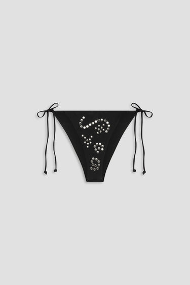 Black bikini bottom with embellishments on a light gray background