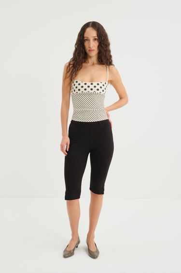 Woman wearing a polka dot top and black capri pants on a white background